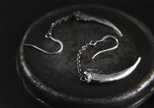 silver claw earrings displayed on a metal surface